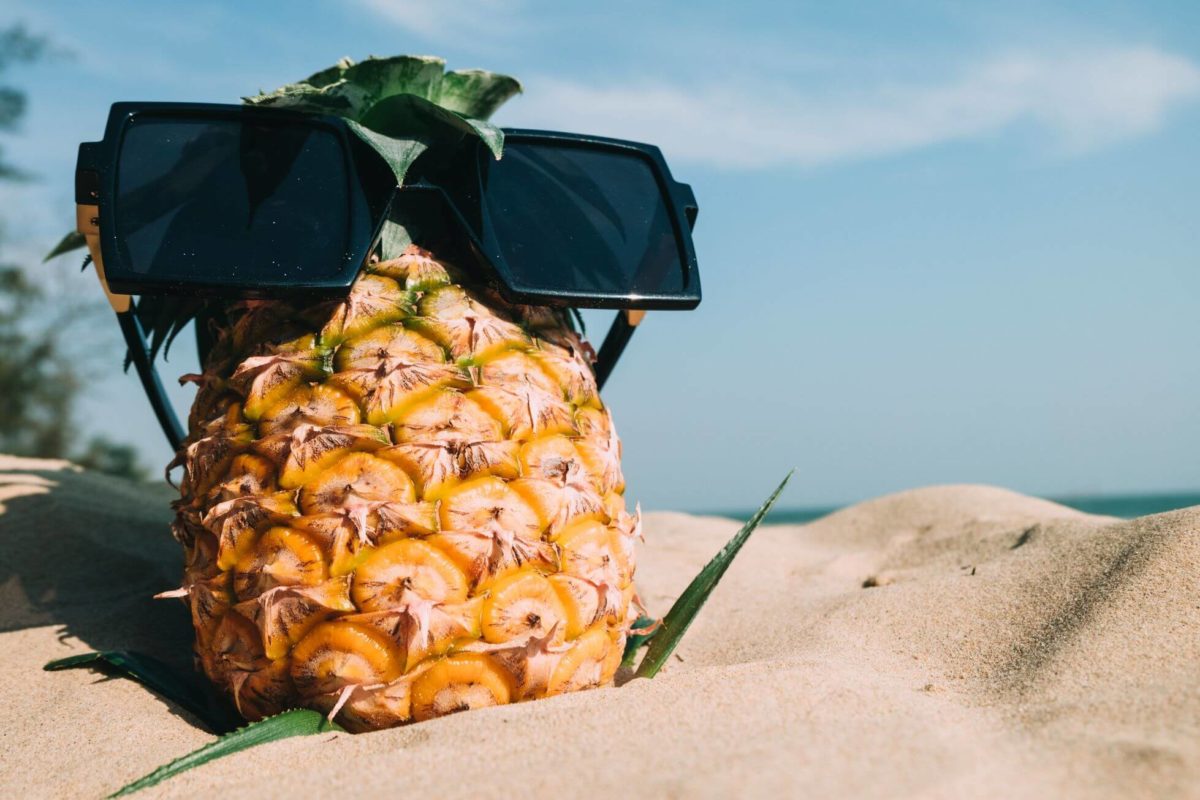 Pineapple with sunglasses in the sand