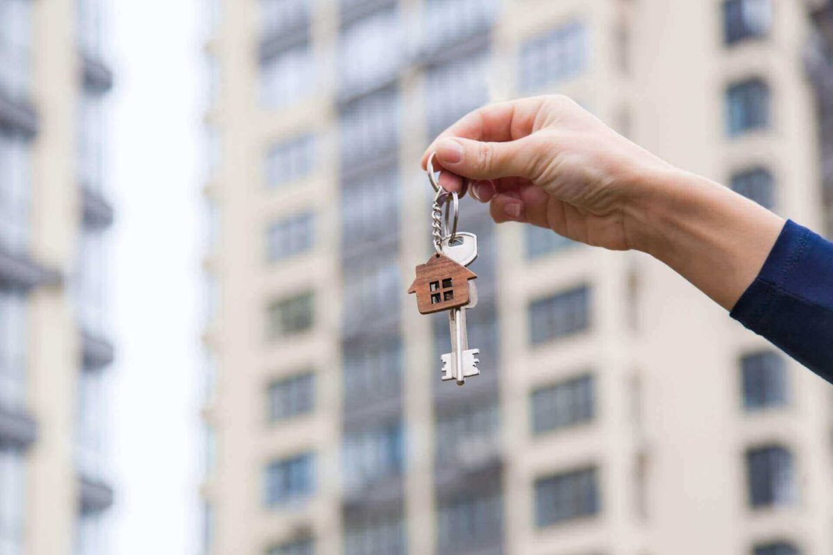 A hand holding house keys in front of a building