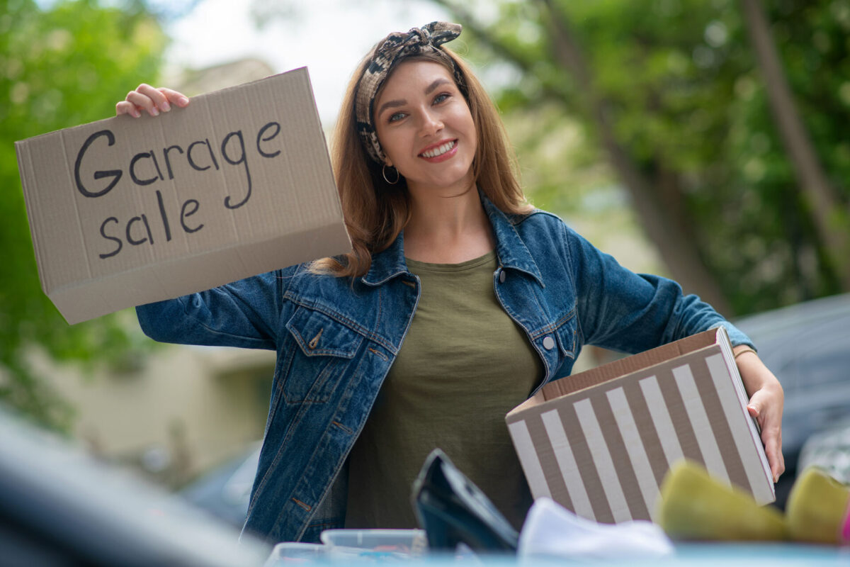 A young girl smiling and holding a sign saying 'garage sale'