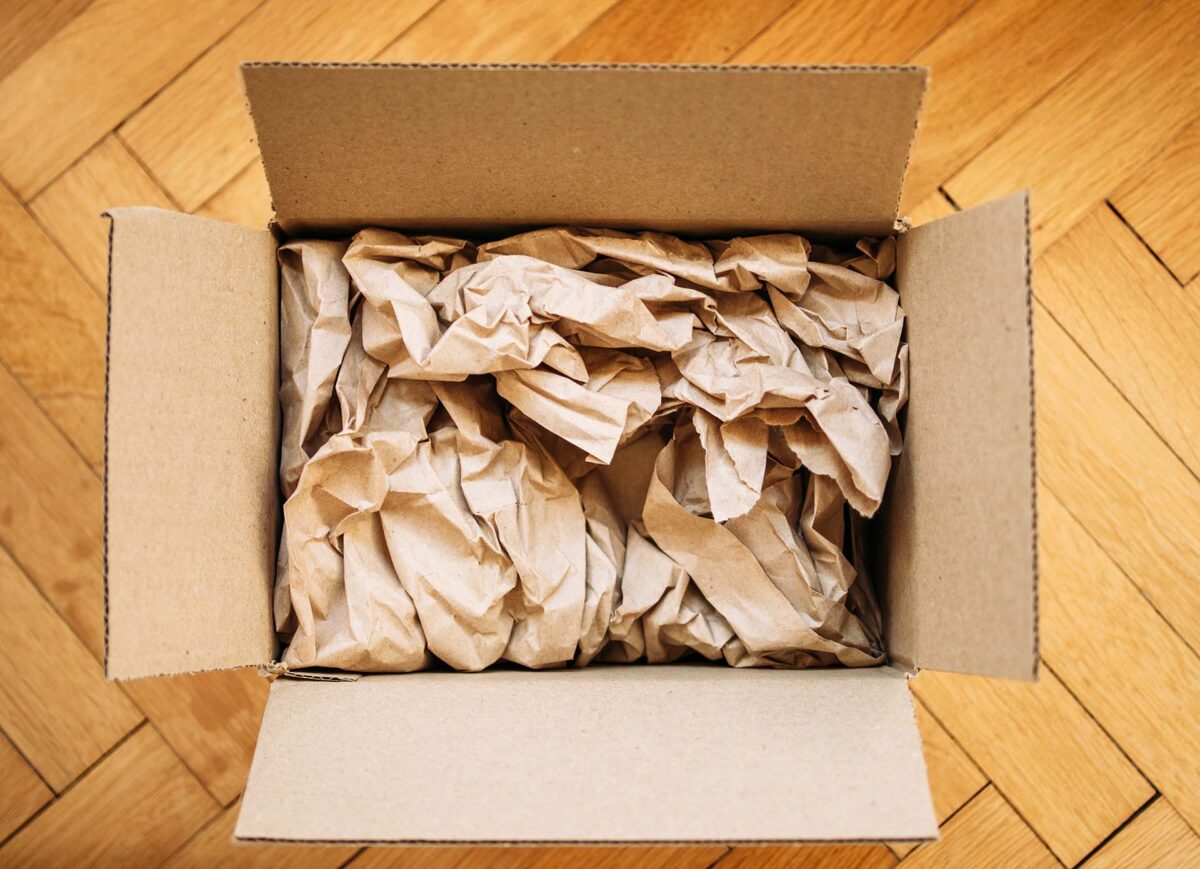Cardboard box filled with shipping packaging paper on a wood floor, seen directly from above. Freight transportation and e-commerce concept